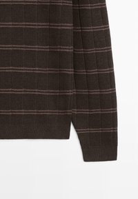 Donkerbruine geribbelde gebreide trui mouw en zoom met dunne horizontale lichtroze strepen op een effen witte achtergrond.