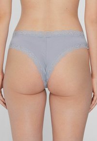 Culotte grise bordée de dentelle avec une texture douce, présentant un bord festonné et un ajustement ajusté. La vue arrière met en valeur les contours et les détails de conception.