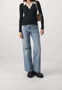 Haut noir côtelé à manches longues avec col crème, associé à un jean large bleu clair et des bottines plateformes à semelles épaisses noires.