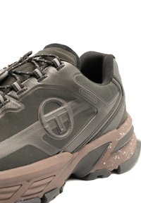 Waterproof dark green sneaker with textured upper, reinforced toe, and brown speckled sole. Features black laces and a logo on the side.