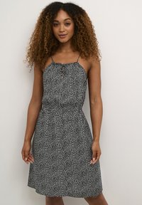 Robe noire et blanche à motifs, avec des bretelles spaghetti, un encolure froncée, une taille cintrée et une jupe évasée. Tissu léger avec une texture lisse.