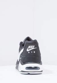 Nike Air Max schoenen met een zwarte bovenkant, witte accenten en zichtbare luchtkussens bij de hiel. Getextureerde stof en rubberen zool.