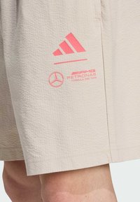 Beige shorts med en texturerad finish. Rosa adidas-logotyp och Mercedes-AMG Petronas-branding finns på undersidan.