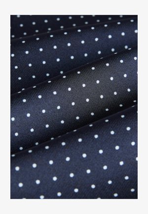 Marinblått tyg med små vita prickar, slät textur, troligtvis gjort av polyester eller siden, vikt i lager.