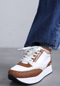 Hvit og brun sneakers med teksturerte brune detaljer, glatt hvitt skinn og en hvit plattformsåle. Har snøring og dekorativ søm.