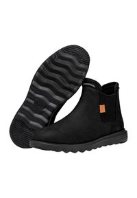 Botas negras de tobillo hechas de cuero texturizado, con paneles laterales elásticos, suela de goma con un diseño ondulado y una etiqueta con el logo en naranja.