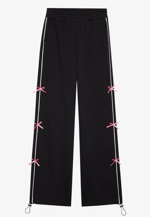 Melni sporta bikses ar plašu kāju dizainu, baltām sānu svītrām un rozā lentei līdzīgām akcents pie apakšmalas. Tām ir elastīga josta un aukliņa.