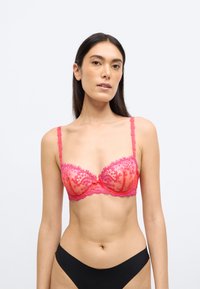 Ροζ δαντελένιο σουτιέν με ημιδιαφανή κύπελλα, λουλουδένια σχέδια και λεπτές τιράντες. Διαθέτει κεντρικό φιόγκο και συνοδεύεται από μαύρο εσώρουχο που ταιριάζει.