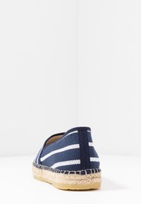 Espadrille i kanvas med marinblå och vita ränder, sula av juterot, platt klack och rundad tå, med en slät yta.