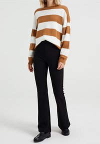 Randig stickad tröja i brun och vit med nedhasade axlar, matchad med svarta utsvängda byxor och svarta skor. Enkelt design, mjuk textur.