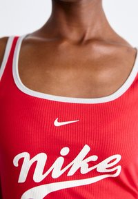 Röd ribbad linne med vit kant och stor "Nike"-logotyp tryckt i vitt. Har en rundad halsringning och en åtsittande design.