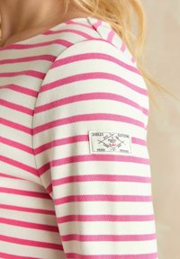 Biało-różowy, w paski, długi rękaw, top z okrągłym dekoltem i naszywką z logo na rękawie. Miękki, bawełnowy materiał, gładka faktura.