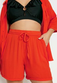 Czerwone szorty z teksturowanej tkaniny z elastycznym paskiem i sznurkiem; w zestawie z czarnym topem crop z falbanami.