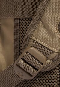 Brązowy pasek do plecaka z nylonu z plastikową klamrą, o teksturze siateczki i wzmocnionym przeszyciem. Zawiera detal z logo marki.