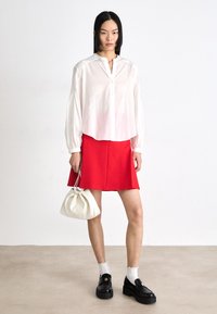 White long-sleeve blouse with a buttoned neckline, paired with a red flared skirt. Accessories include a white handbag and black platform shoes.