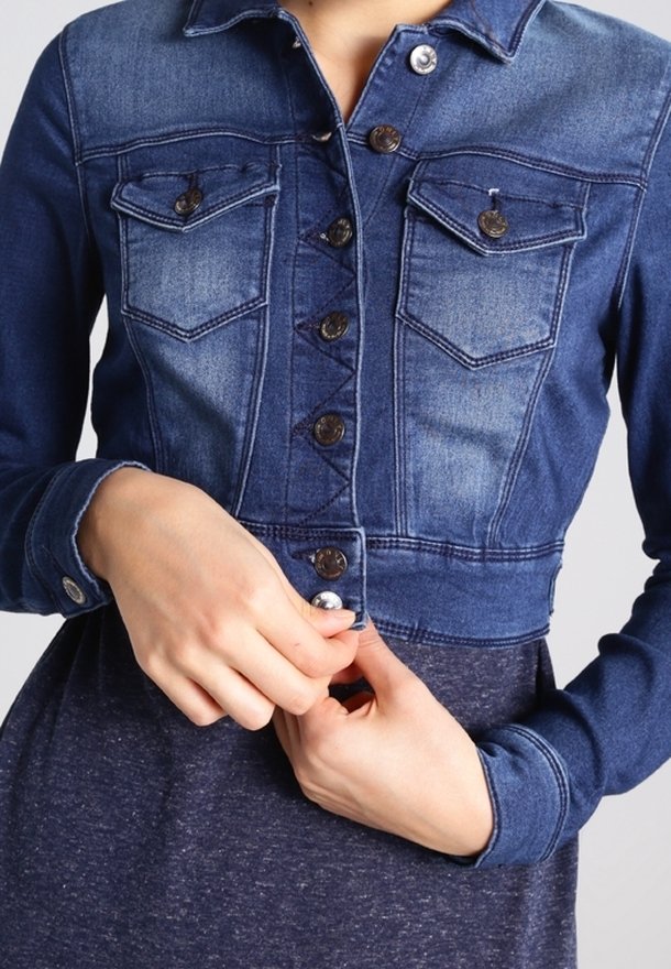 Denim cropped jacket in dark blue, featuring button closure, two chest pockets, distinct stitching, and a soft texture.