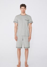 Conjunto de pijama de algodón gris de manga corta que presenta un bolsillo en la camiseta y un borde negro en las mangas y los pantalones cortos, ofreciendo un ajuste relajado.