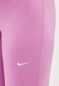 Κοντινό πλάνο ροζ αθλητικού κολάν με λευκό λογότυπο Nike στην κορυφή του μηρού και ορατή ραφή.