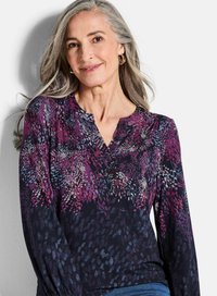 Langsleeve shirt in het donker met een bloemenpatroon in tinten paars, roze en blauw. Het heeft een v-halslijn en geplooide details op de mouwen.