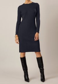 Abito a maglia a coste navy con maniche lunghe, scollatura rotonda e spacco laterale, abbinato a stivali neri al ginocchio con punta.