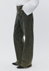 Vidbenede jeans i mørkegrønt denim, der har høj talje, bæltestropper og en afslappet pasform. Stylet med spidse sorte sko.