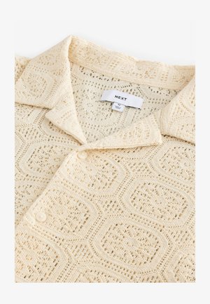 Kermanvalkoinen neulepaita, jossa on geometrinen mehiläisen kennokuvio, pehmeä pinta, kauluksellinen kaula-aukko ja napillinen suljenta.