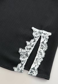 Crni teksturirani materijal s bijelim čipkastim akcentom koji sadrži cvjetne uzorke i detalj izreza u obliku ključa s jedne strane.