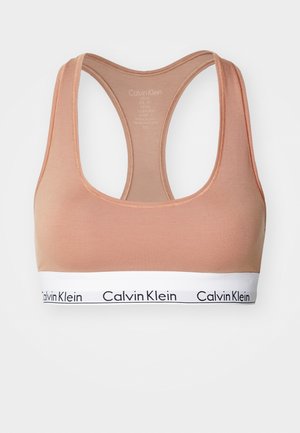 Light peach sports bra made of stretchy material, featuring a wide white band with black "Calvin Klein" logo and racerback design.