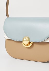 Sac à main en color-block, avec un rabat en cuir bleu clair, un corps en beige et un matériel circulaire doré avec un fermoir. Texture lisse dans l'ensemble.