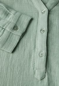 Camicia in lino verde chiaro con patta dei bottoni, tessuto strutturato e polsini ripiegati con chiusura a bottone singolo.