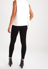 Top blanco sin mangas con tejido texturizado, combinado con jeans skinny negros y zapatos de tacón alto negros, visto desde atrás.