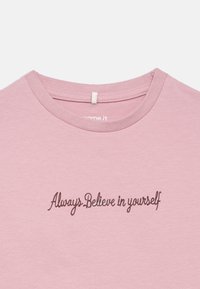 Camisa de gola redonda rosa claro com texto em cursivo escuro a dizer "Acredita sempre em ti" centrado no peito.