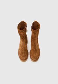 Bottines en suède marron avec une texture lisse, un design légèrement lâche et des fermetures éclair sur les côtés. Coutures renforcées autour des semelles.