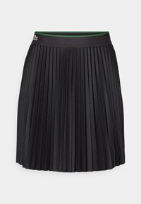 Jupe plissée noire avec taille élastique, comportant un petit logo crocodile sur le côté gauche et une doublure intérieure verte au niveau de la taille.