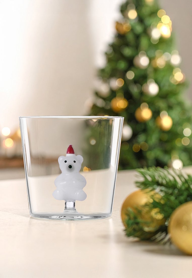 Durchsichtiger Glasbecher mit einer weißen Eisbärfigur mit rotem Hut am Boden, umgeben von einem Weihnachtsbaum und Schmuck.