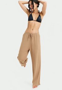 Calças largas, leves e bege com cintura elástica. Textura suave e detalhe de bainha desfiada. Usadas acima do tornozelo.