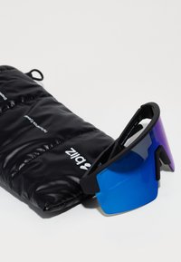 Gafas de sol deportivas negras con una gran lente en degradado azul. Acompañadas de un estuche acolchado negro con detalles de marca en blanco.