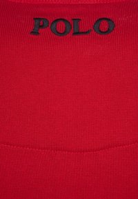 Tissu tricoté rouge avec texte brodé "POLO" en noir près du bord supérieur.