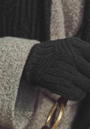 Black knitted glove with ribbed texture, holding a gold circular accessory, paired with a light gray textured coat.