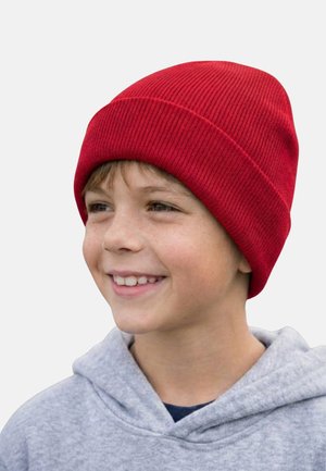 Smiling child wearing a bright red knit beanie and a light gray hoodie, looking slightly to the right on a neutral background.