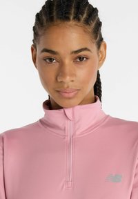 Helles rosa, langärmliges, hochgeschlossenes Sportoberteil mit einem Viertel-Reißverschluss und kleinem grauen Logo auf der linken Seite. Glattes, dehnbares Material.