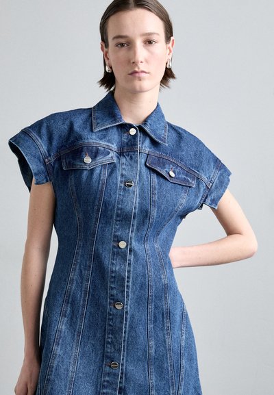 Rochie din denim cu mâneci scurte, design ajustat, nasturi la front, două buzunare la piept și detalii subtile de cusătură. Culoare albastru închis și textură netedă.