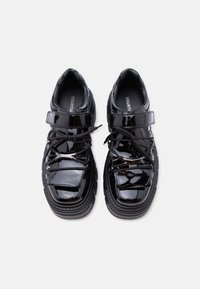 Μαύρα sneakers από λουστρινι δέρμα με χοντρή σόλα, διαθέτουν στεφάνη σύσφιξης μπροστά και κορδόνια, υφή με ανάγλυφο φινίρισμα και λογότυπο στην εσωτερική σόλα.