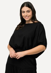 Haut noir à manches courtes avec un design ample et froncé à la taille. Fabriqué en tissu lisse, il présente un col large et des poignets élastiques.