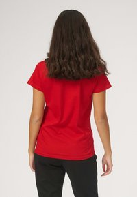 Rød bomulds T-shirt med rund hals og korte ærmer, vist fra den ene side, har en glat tekstur og en afslappet pasform.