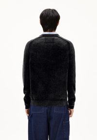 Schwarzer Strickpullover mit strukturierter Oberfläche, geripptem Kragen und Bündchen. Verfügt über ein rechteckiges Rückenetikett und eine taillierte Passform.
