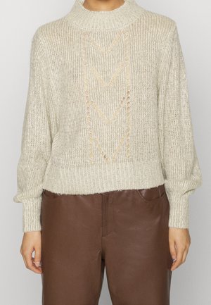 Pull en maille crème avec motif ajouré chevron, associé à un pantalon en cuir marron taille haute, présenté des épaules aux hanches.