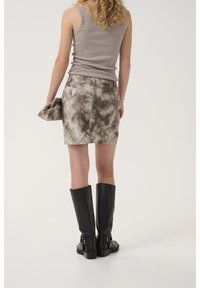 Top grigio abbinato a una mini gonna a tie-dye marrone. L'outfit è completato da stivali alti neri in pelle.