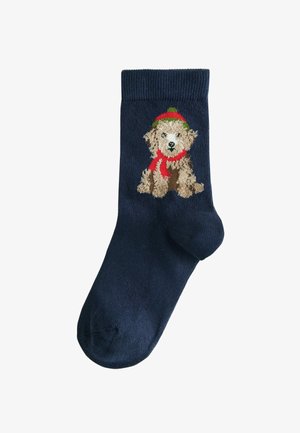 Tums zilas kokvilnas zeķes, kurām ir teksturēts izšūts suns ar sarkanu šalli un zaļu cepuri. Ribota piedurkne, ar vienkāršu krāsas ķermeni.