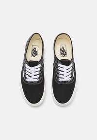Svarte lerrets sneakers med hvite snøring og rutete detalj. Har en klassisk lav topp-design og gummisåle.